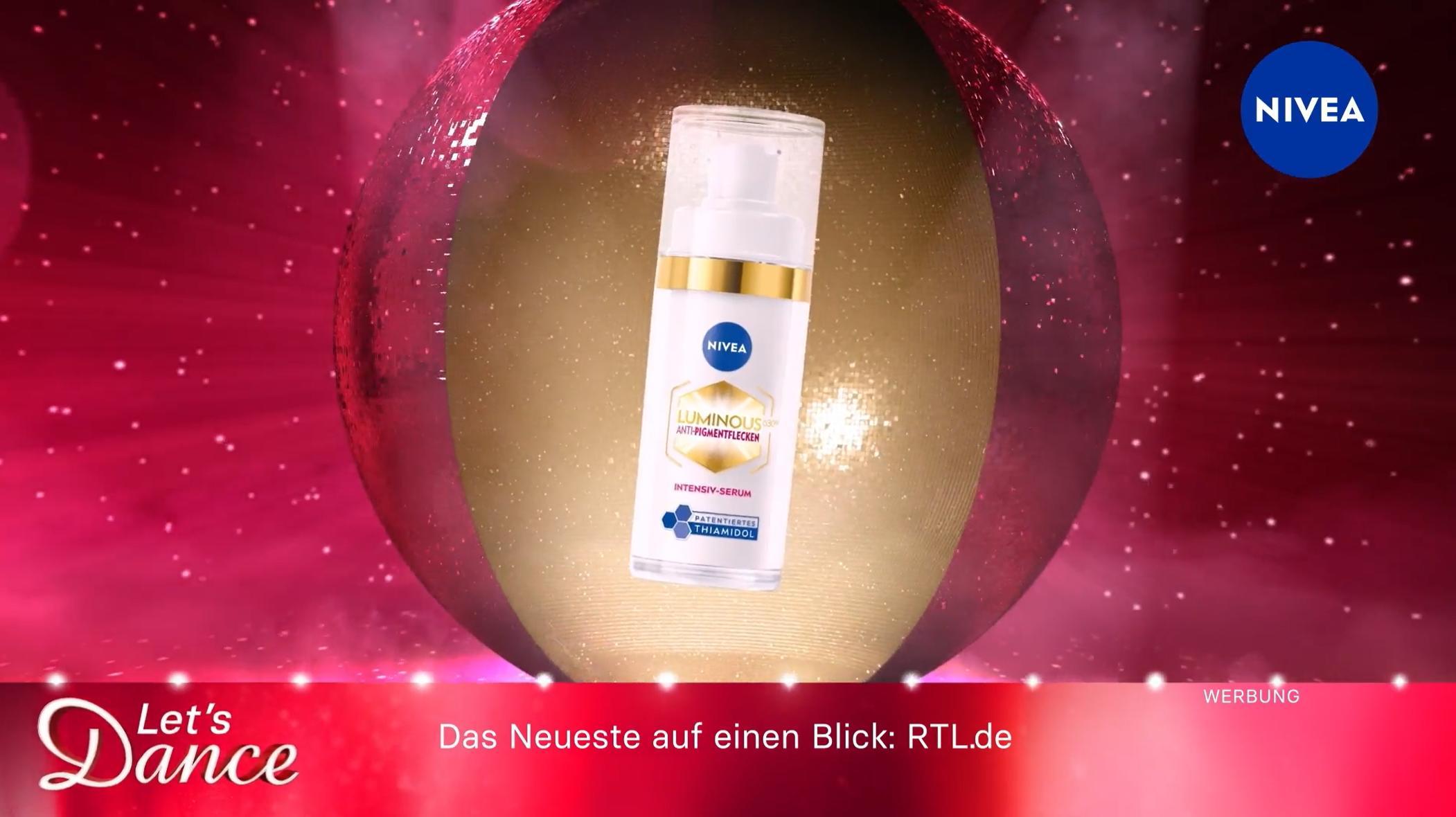 Das Bild zeigt eine Werbung für ein Nivea-Produkt im Rahmen der Sendung 'Let's Dance'. Ein Nivea Luminous630 Anti-Pigmentflecken-Serum ist in der Mitte des Bildes dargestellt, umgeben von glitzerndem, rotem Hintergrund. Oben rechts ist das Nivea-Logo sichtbar. Unten links ist das Logo von 'Let's Dance' abgebildet, und darunter der Hinweis auf weitere Informationen auf RTL.de. Die gesamte Szenerie wirkt glamourös und festlich.
#!#
Nivea,Let's Dance,Werbung,RTL,Kosmetik,Serum,Anti-Pigmentflecken,Glamour,Hautpflege,TV