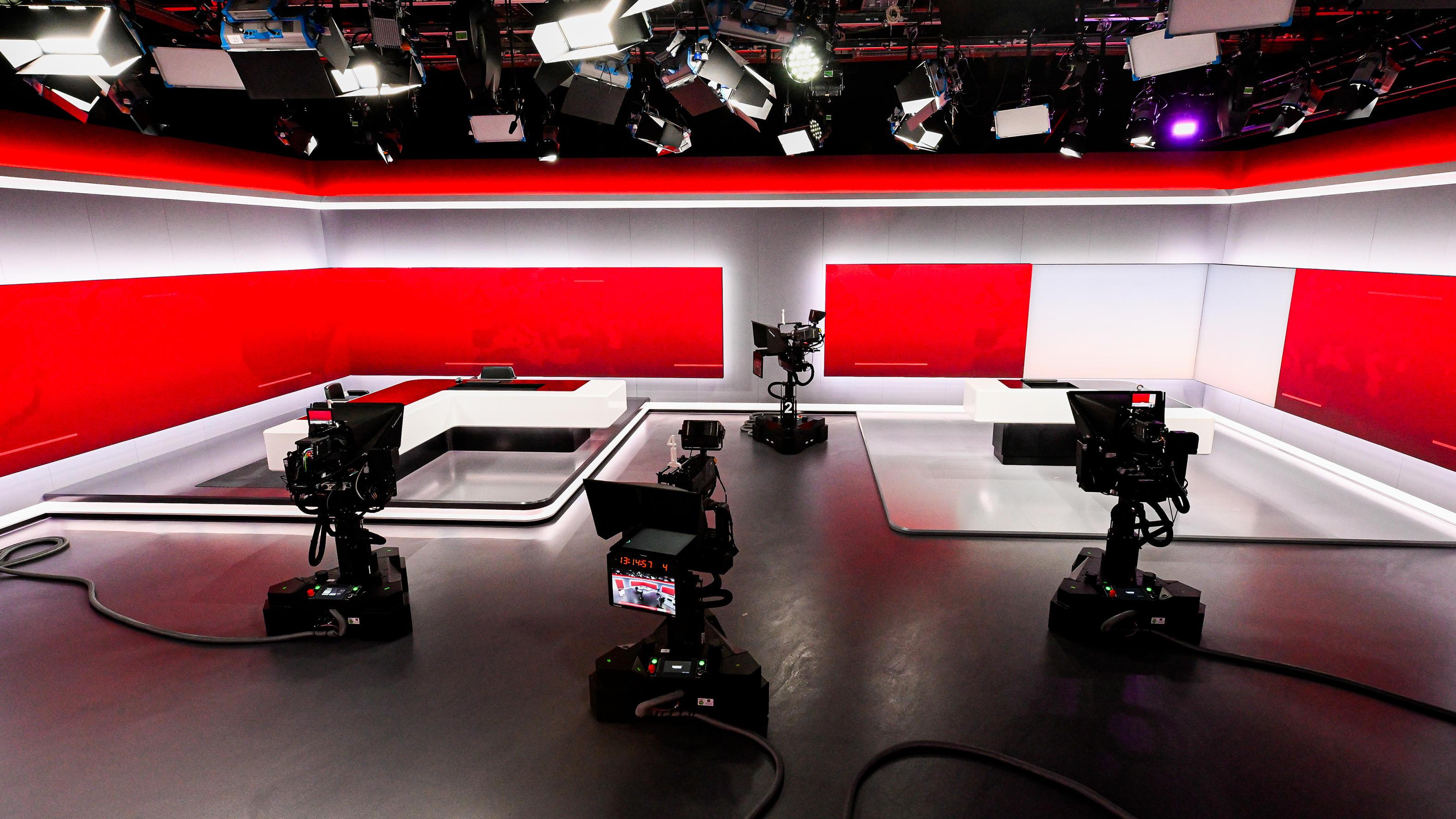 Das Bild zeigt ein modernes Fernsehstudio, das mit mehreren professionellen Kameras ausgestattet ist. Der Raum ist in neutralen Farben gehalten, mit dominierenden roten und weißen Elementen an den Wänden und auf den Bildschirmen. Die Decke ist mit zahlreichen Beleuchtungen und technischen Ausrüstungen versehen, die den Raum gleichmäßig ausleuchten. Auf dem Boden sind Kabel sichtbar, die die Kameras mit den entsprechenden Systemen verbinden. Der Raum wirkt aufgeräumt und bereit für eine Live-Übertragung oder Aufnahme.
#!#
Fernsehstudio,Kameras,Beleuchtung,Aufnahme,Technik,Live-Übertragung,Rot,Weiß,Neutral,Professionell