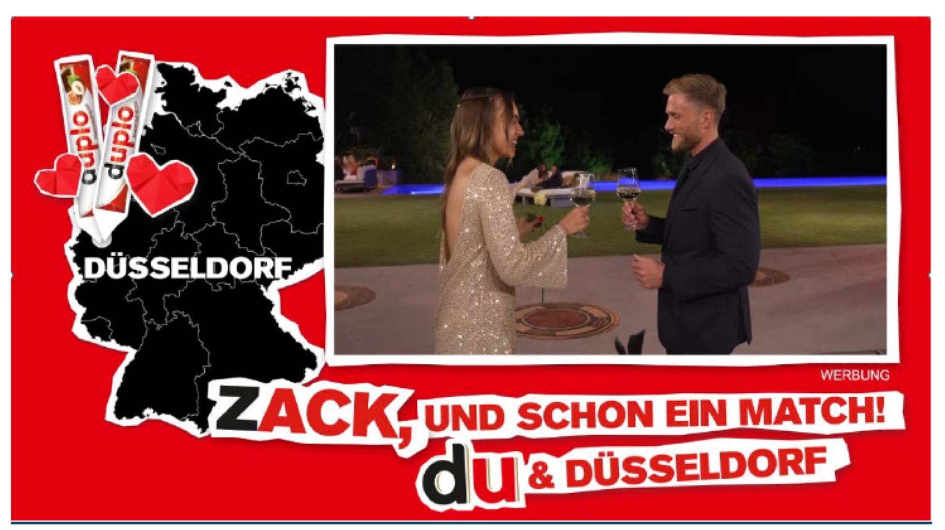 Das Bild zeigt eine Werbung mit einem roten Rahmen, die eine romantische Begegnung in Düsseldorf darstellt. Im Vordergrund ist ein Paar zu sehen, das sich draußen bei Nacht bei einem Glas Sekt anstößt. Die Frau trägt ein glänzendes, elegantes Kleid und der Mann einen dunklen Anzug. Links ist eine Karte von Deutschland mit der Hervorhebung von Düsseldorf abgebildet. Darüber sind zwei Duplo-Schokoriegel und Herzen zu sehen. Der Text 'Zack, und schon ein Match! du & Düsseldorf' ist prominent in der Mitte platziert.
#!#
Werbung,Düsseldorf,Romantik,Duplo,Deutschland,Paar,Nacht,Sekt,Begegnung,Herzen