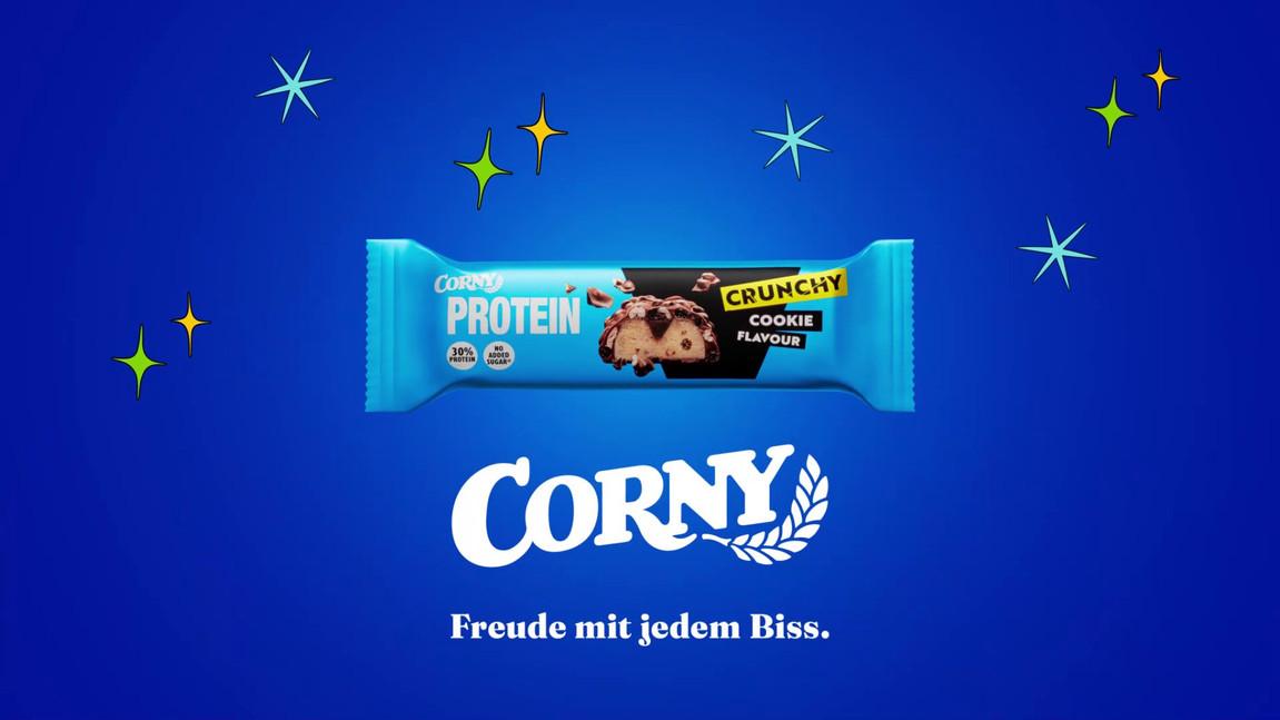 Corny Proteinriegel vor blauem Hintergrund mit Sternen und Text 'Freude mit jedem Biss.'