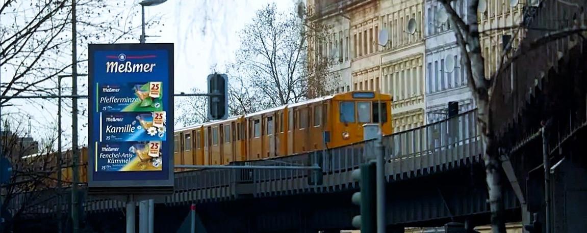 Gelbe U-Bahn auf Hochbahn und Meßmer-Werbeplakat im Vordergrund.