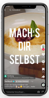 Das Bild zeigt ein Smartphone, auf dem ein Video abgespielt wird. Im Vordergrund ist eine Nahaufnahme eines Tellers mit Grießbrei zu sehen. Auf dem Grießbrei befinden sich eine rote Fruchtsauce und ein grünes Minzblatt als Dekoration. Der Bildschirm zeigt den Text 'MACH'S DIR SELBST', was dazu anregen soll, das Gericht selbst zuzubereiten. Die Benutzeroberfläche des Smartphones zeigt typische soziale Medien-Interaktionsmöglichkeiten wie Likes und Kommentare.
#!#
Grießbrei,Rezept,Selbstgemacht,Kochvideo,Fruchtsauce,Minze,Social Media,Smartphone,Kochen,Anleitung