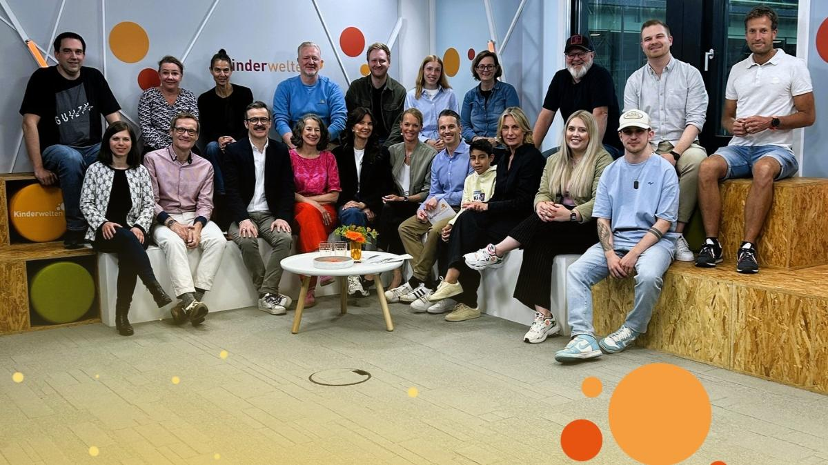 Das Bild zeigt eine Gruppe von Menschen, die auf einer Bühne sitzen und stehen. Der Hintergrund ist mit dem Logo von 'Kinderwelten' dekoriert. Die Teilnehmer sind lächelnd und in entspannter Atmosphäre. Die Bühne ist mit Holzpodesten und einer Tischdekoration versehen, die aus Blumen besteht. Der Raum ist modern gestaltet und verfügt über professionelle Beleuchtung.
#!#
Kinderwelten,Veranstaltung,Gruppenfoto,Bühne,Logo,Teilnehmer,Blumen,Dekoration,Beleuchtung,Atmosphäre